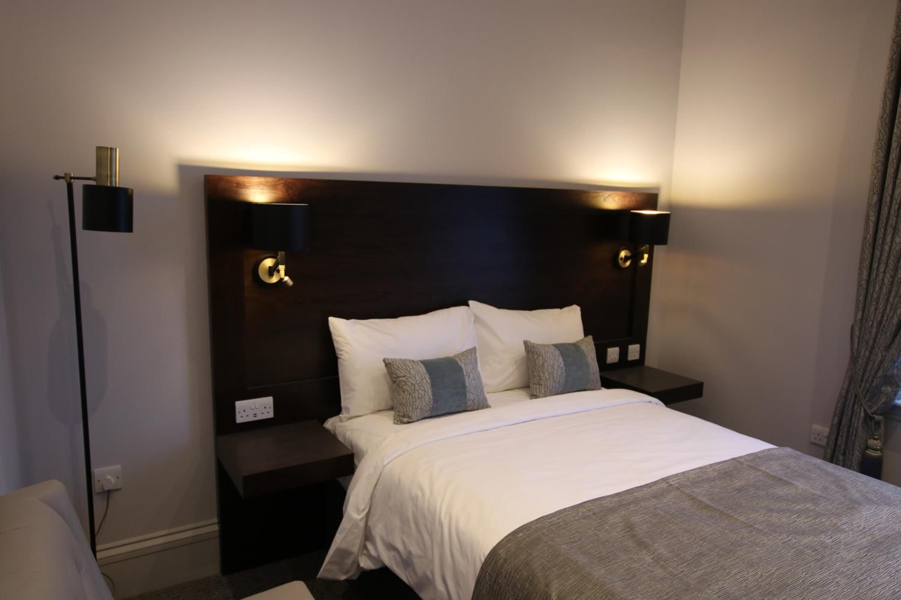 A hotel room with a large bed, two bedside tables, and wall-mounted lamps.