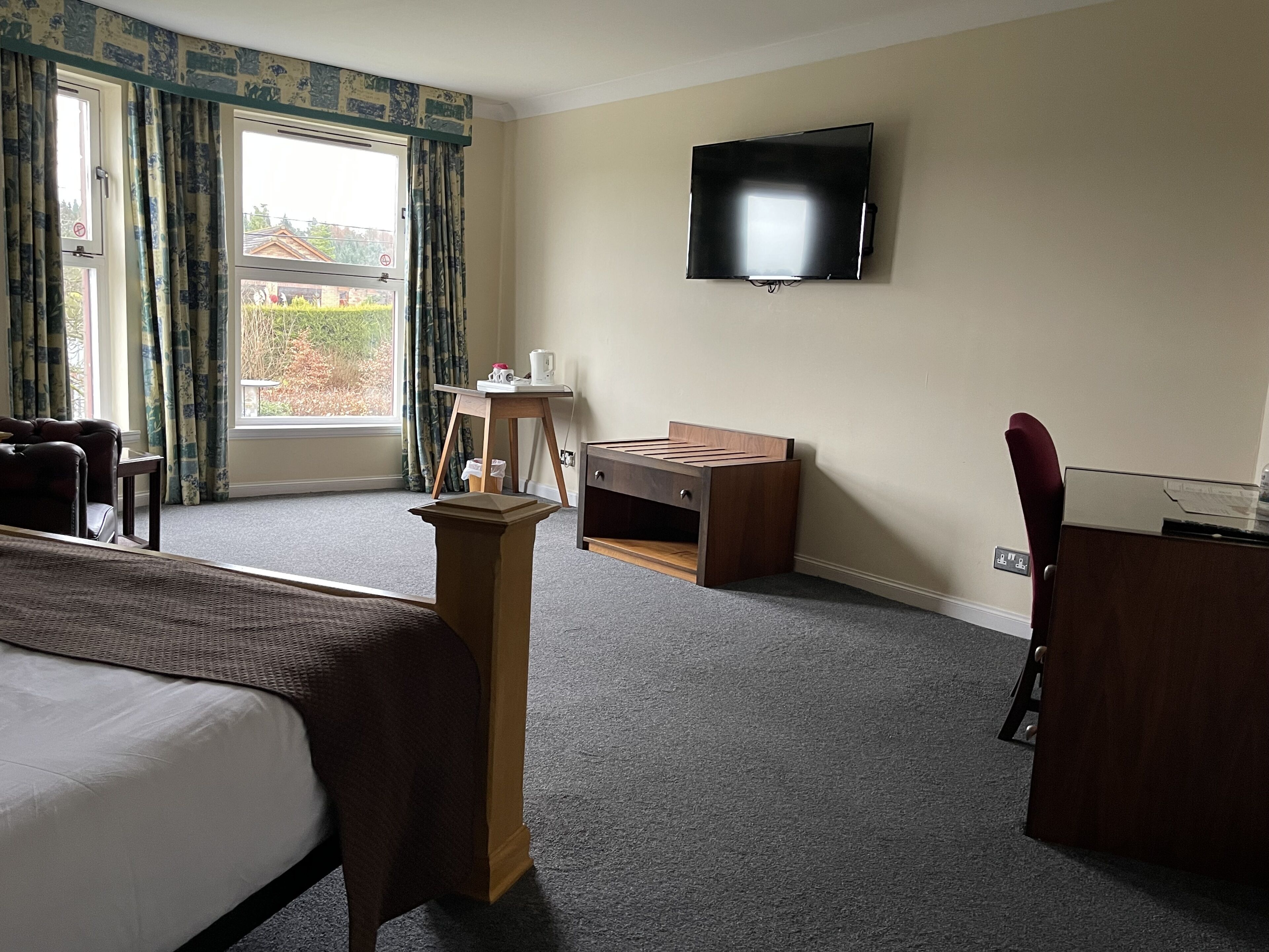 Een hotelkamer met een bed, een bureau, een stoel, een televisie en een raam met gordijnen.