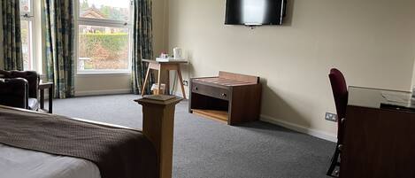 A hotel room with a bed, a desk, a chair, a television, and a window with curtains.