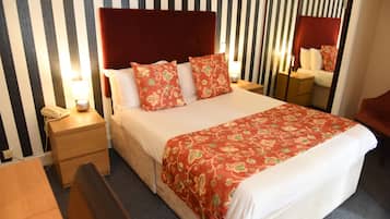Una habitación de hotel con cama, mesitas de noche, lámpara, teléfono y espejo.