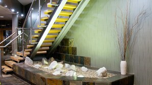 Uma escadaria interna moderna com corrimão de vidro, um vaso de pedra com pedras e um arranjo de galhos.