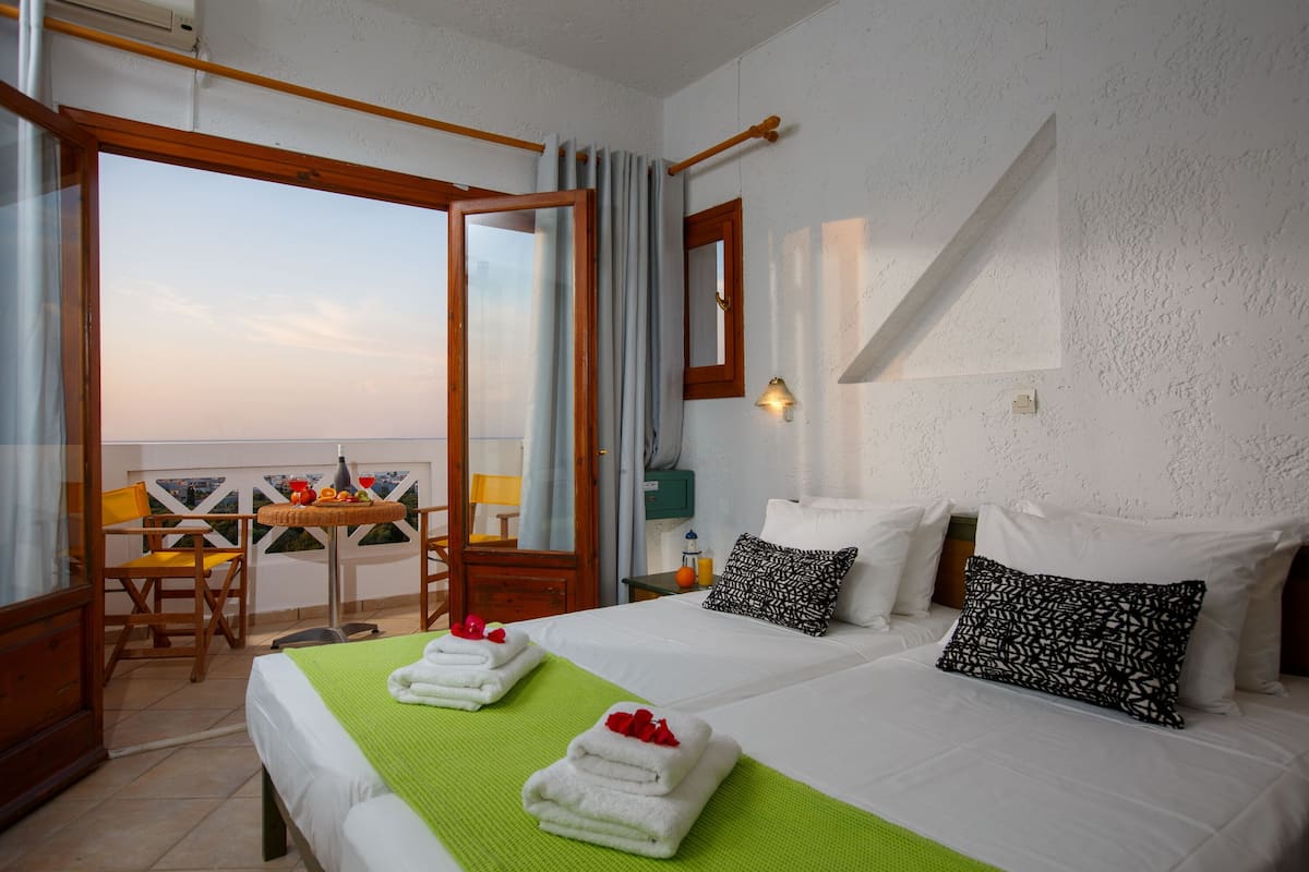 Hotelkamer met een bed, twee kussens, een groene deken, een tafel met een stoel en uitzicht door een glazen deur.