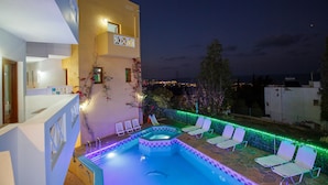 Une piscine avec des chaises longues et une vue sur la ville la nuit.