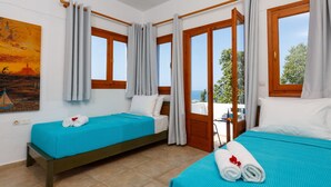 Une chambre d’hôtel avec deux lits, un tableau au mur et une vue sur la mer par les fenêtres.