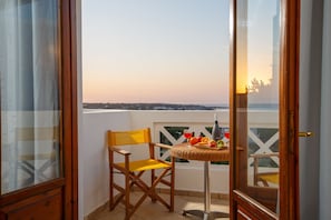 A balcony with a wicker table, a chair, and a view of the cityscape. - Romantica Hotel Apartments (Hersonissos)