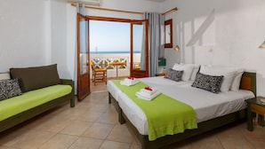 Une chambre d’hôtel avec un lit, un canapé vert, un balcon avec une table et des chaises, et une vue sur la mer.