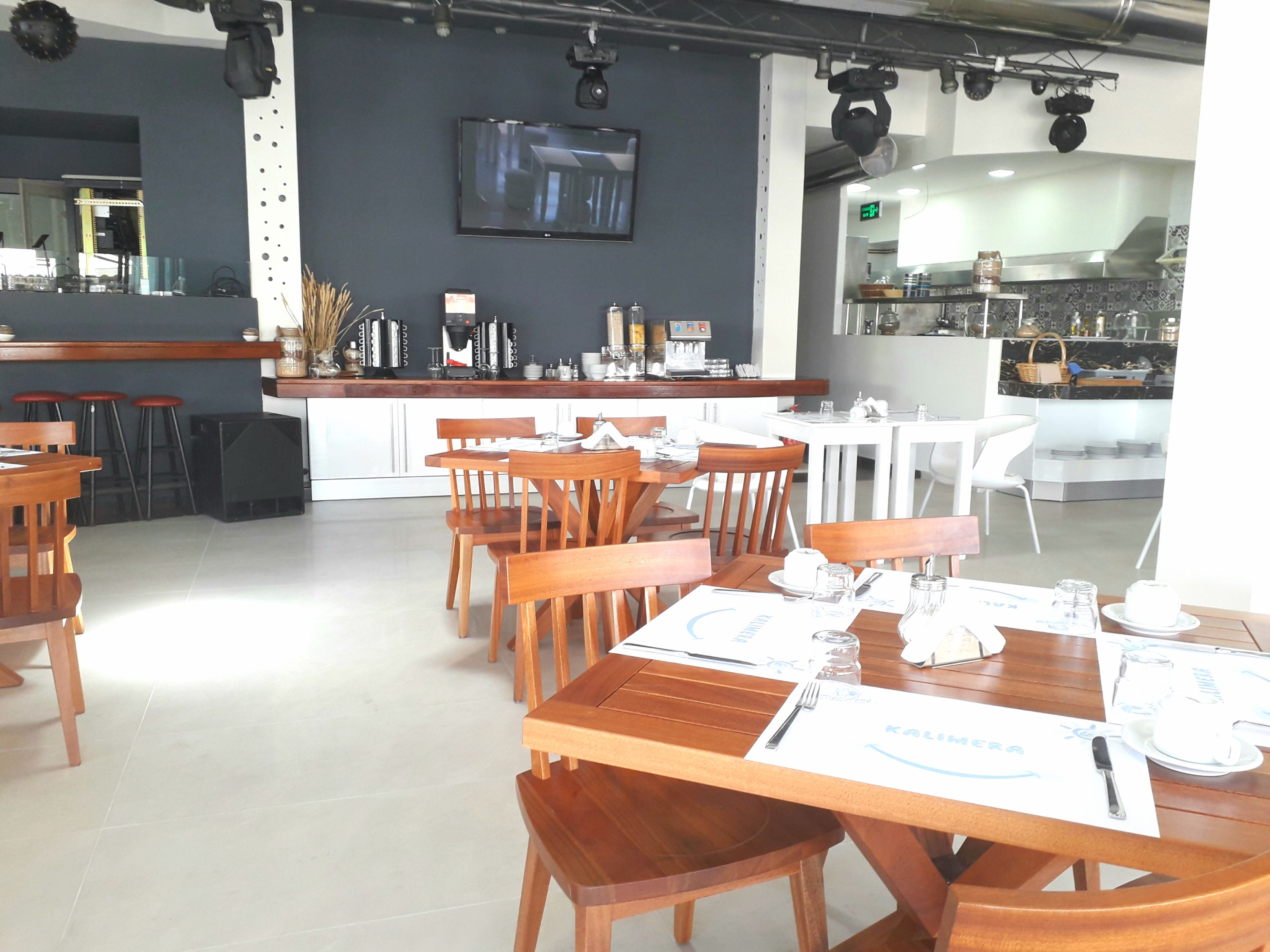 A restaurant with wooden tables and chairs, a bar area, and a kitchen visible in the background.