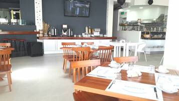 A restaurant with wooden tables and chairs, a bar area, and a kitchen visible in the background.