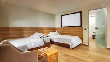 A hotel room with two beds, a wooden headboard, a small wooden table, and a glass door leading to a bathroom.