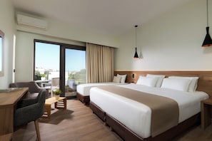 Habitación de hotel con dos camas, un escritorio, una silla, una mesita con una planta y un gran ventanal con cortinas.