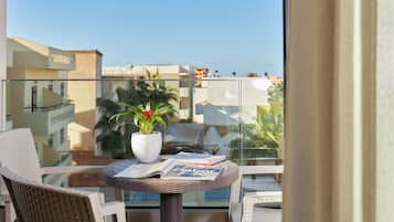 A balcony with wicker chairs, a small table with a potted plant and magazines, and a view of buildings and palm trees.