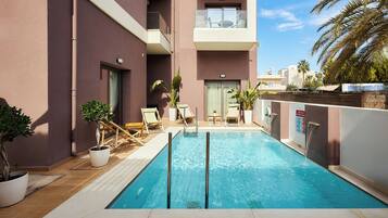 A swimming pool with a wooden deck, lounge chairs, and potted plants.