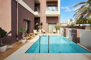 A swimming pool with a wooden deck, lounge chairs, and potted plants. - Dionisos Hotel (Hersonissos)