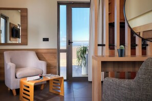 Uma sala de estar moderna com um sofá, uma pequena mesa de madeira, uma TV fixada na parede e vista para o exterior através de uma porta de vidro.