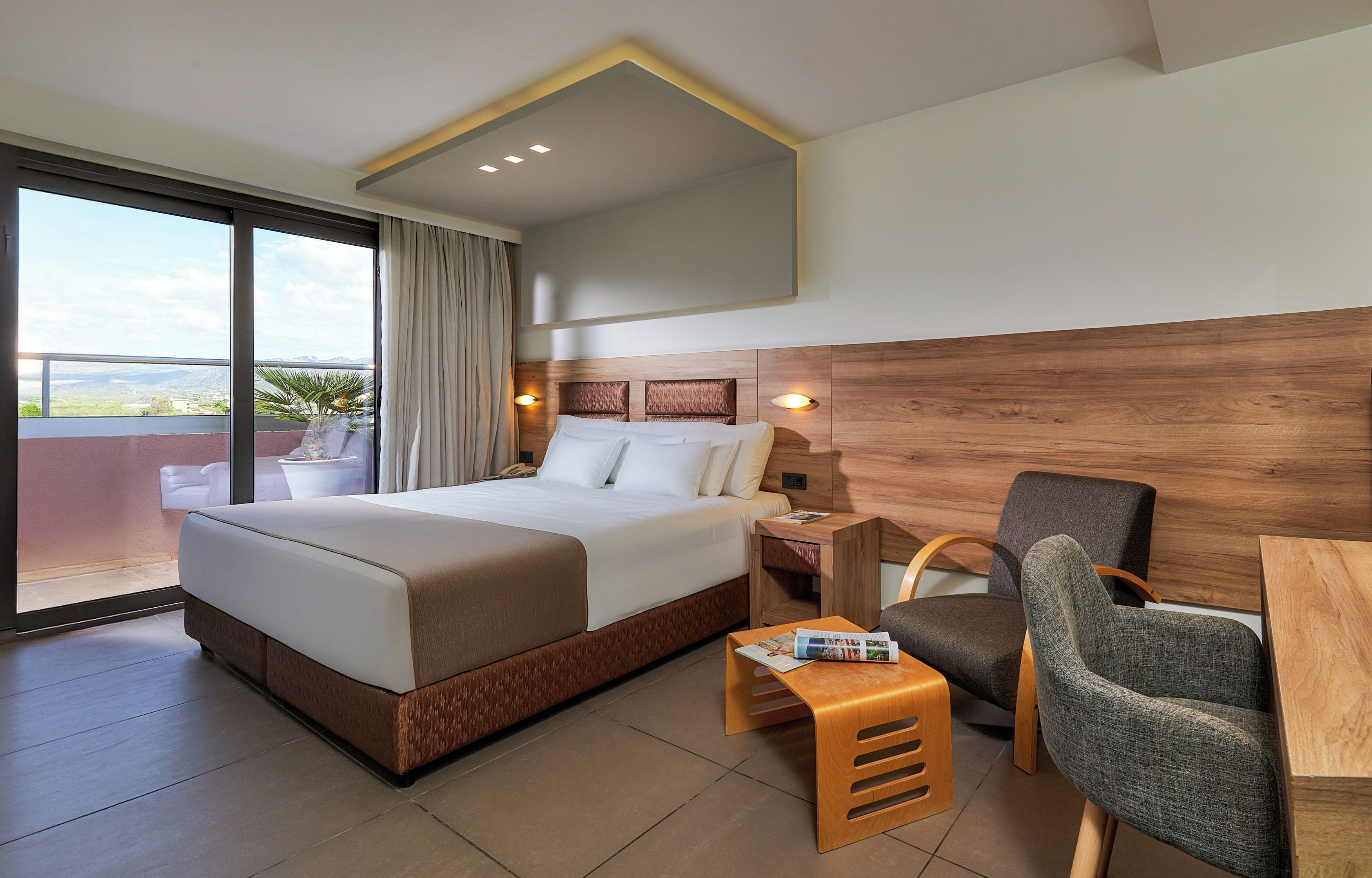 A hotel room with a large bed, a desk, a chair, and a view of the city.