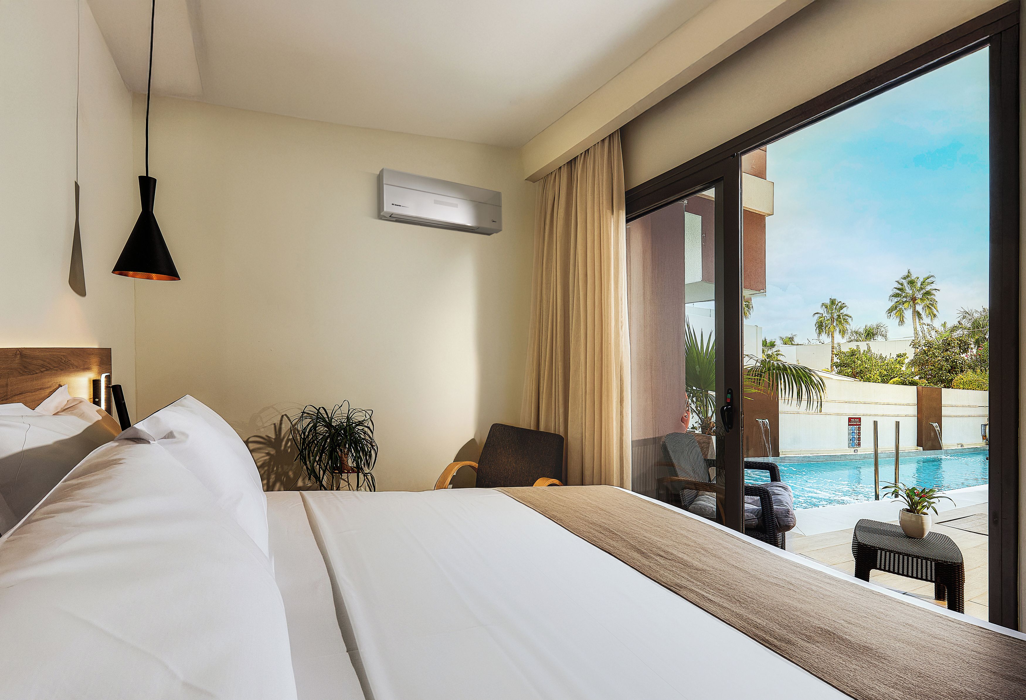 Habitación de hotel con una cama grande, un escritorio, una silla, una planta en maceta y vista a una piscina.