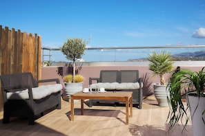 A rooftop terrace with wicker furniture, a wooden table, potted plants, and a view of the sea. - Dionisos Hotel (Hersonissos)