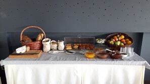 A buffet table with various food items, including bread, pastries, and fruits. - Dionisos Hotel (Hersonissos)