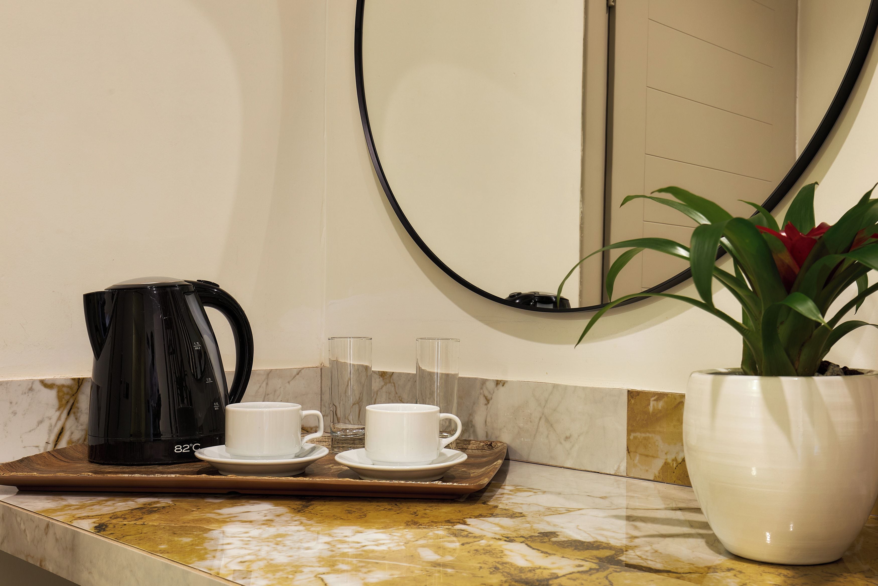 A coffee station with a black coffee maker, two white cups, and a tray on a marble countertop.