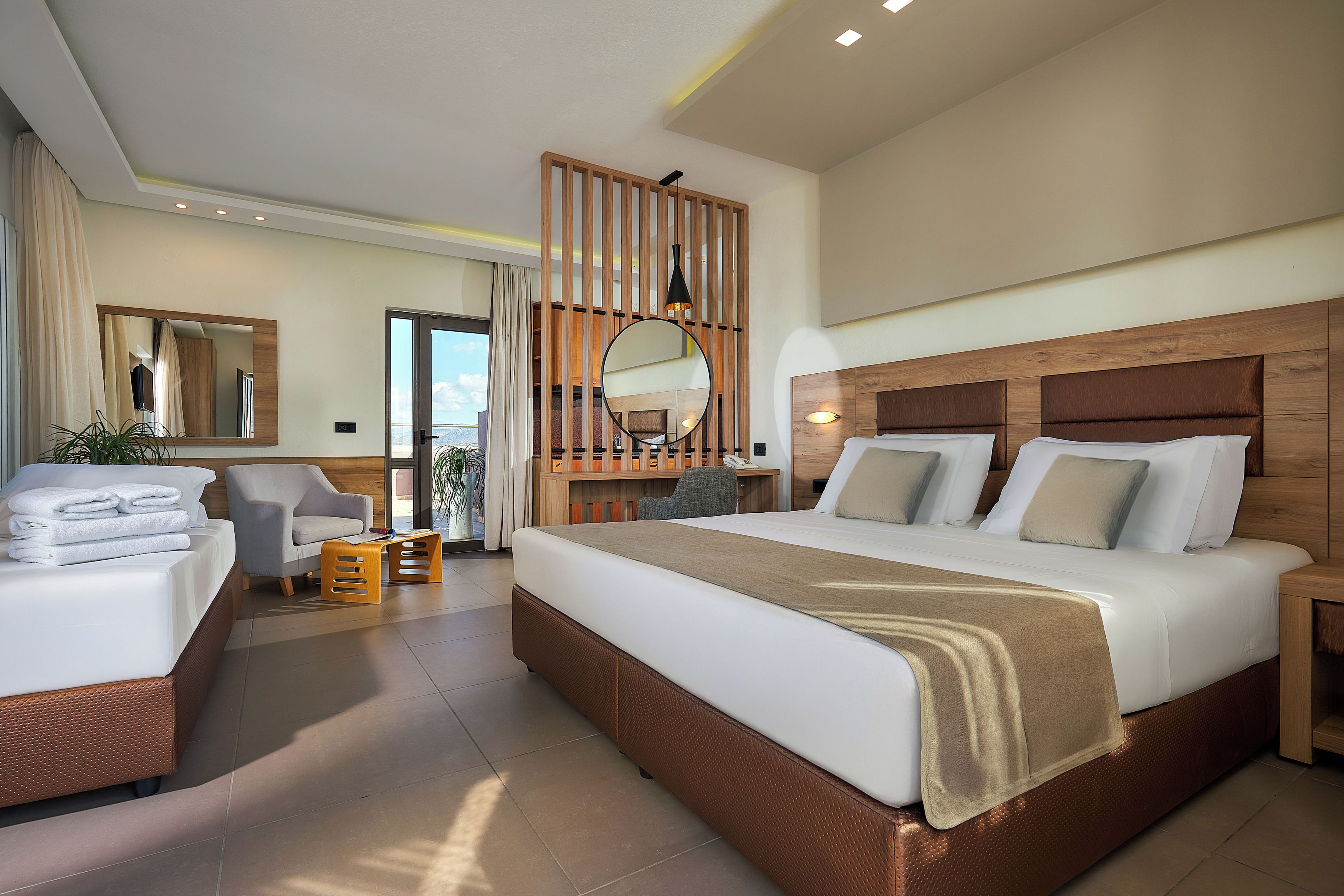 A modern hotel room with a large bed, a desk, and a chair. There is a large mirror and a window with curtains.