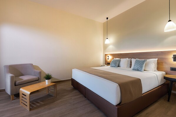 A modern hotel room with a large bed, a sofa, a small table, and a potted plant.