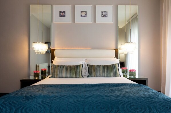 A neatly made bed with a blue patterned bedspread, a white headboard, and a decorative pillow. There are three framed pictures on the wall above the bed.