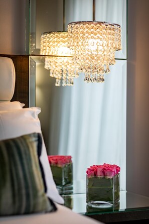 A bedroom with a large mirror, a chandelier, and a vase with pink roses on a bedside table.