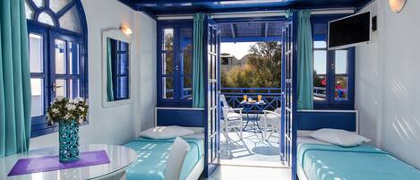 A room with two beds, a table with a vase, and a balcony with a table and chairs.