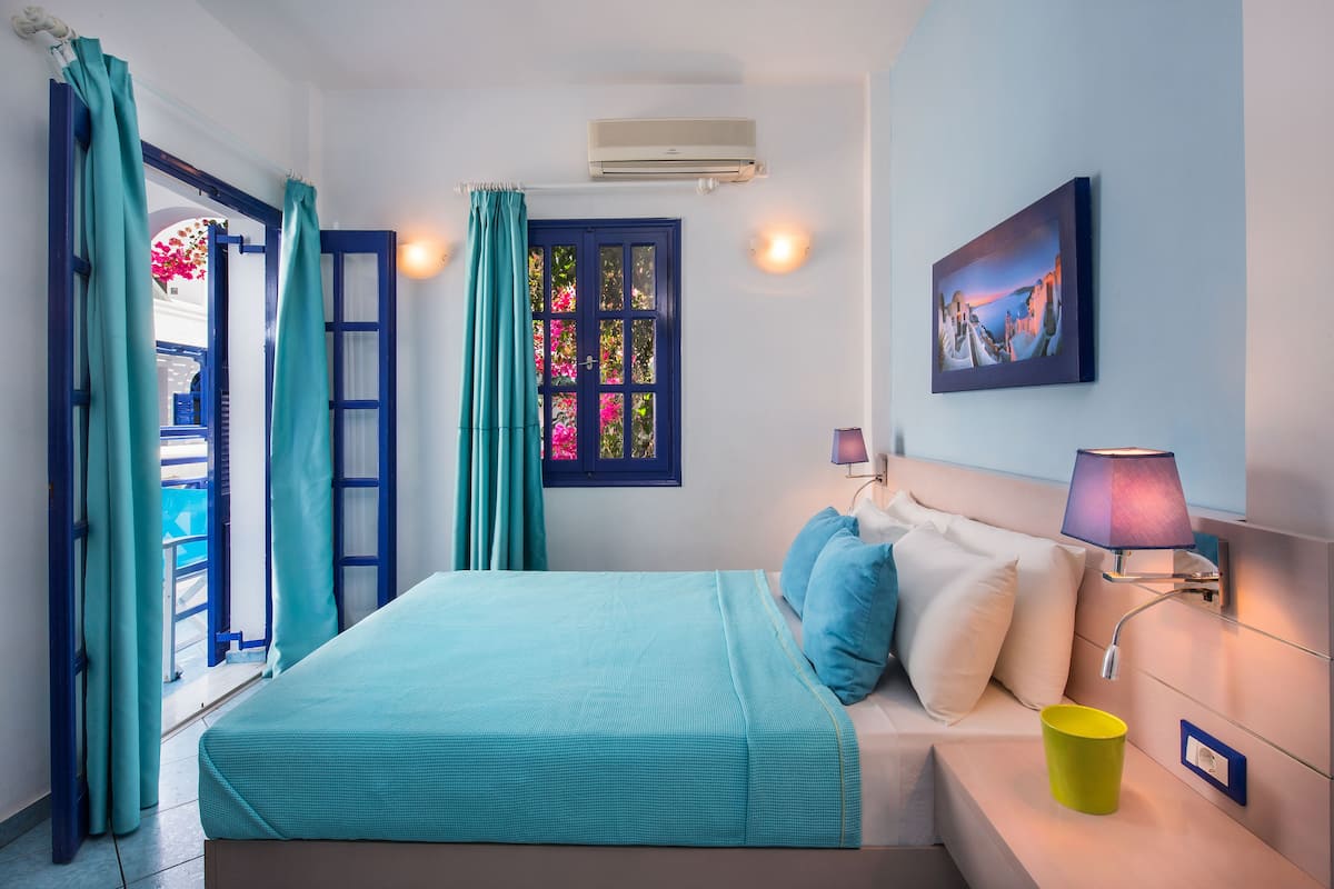 Un dormitorio con una cama, una lámpara de noche, un aire acondicionado instalado en la pared y una ventana con cortinas.