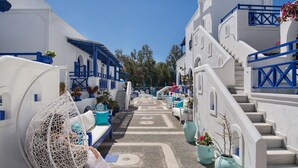 A narrow street with white buildings and blue accents, a hanging chair, and potted plants.