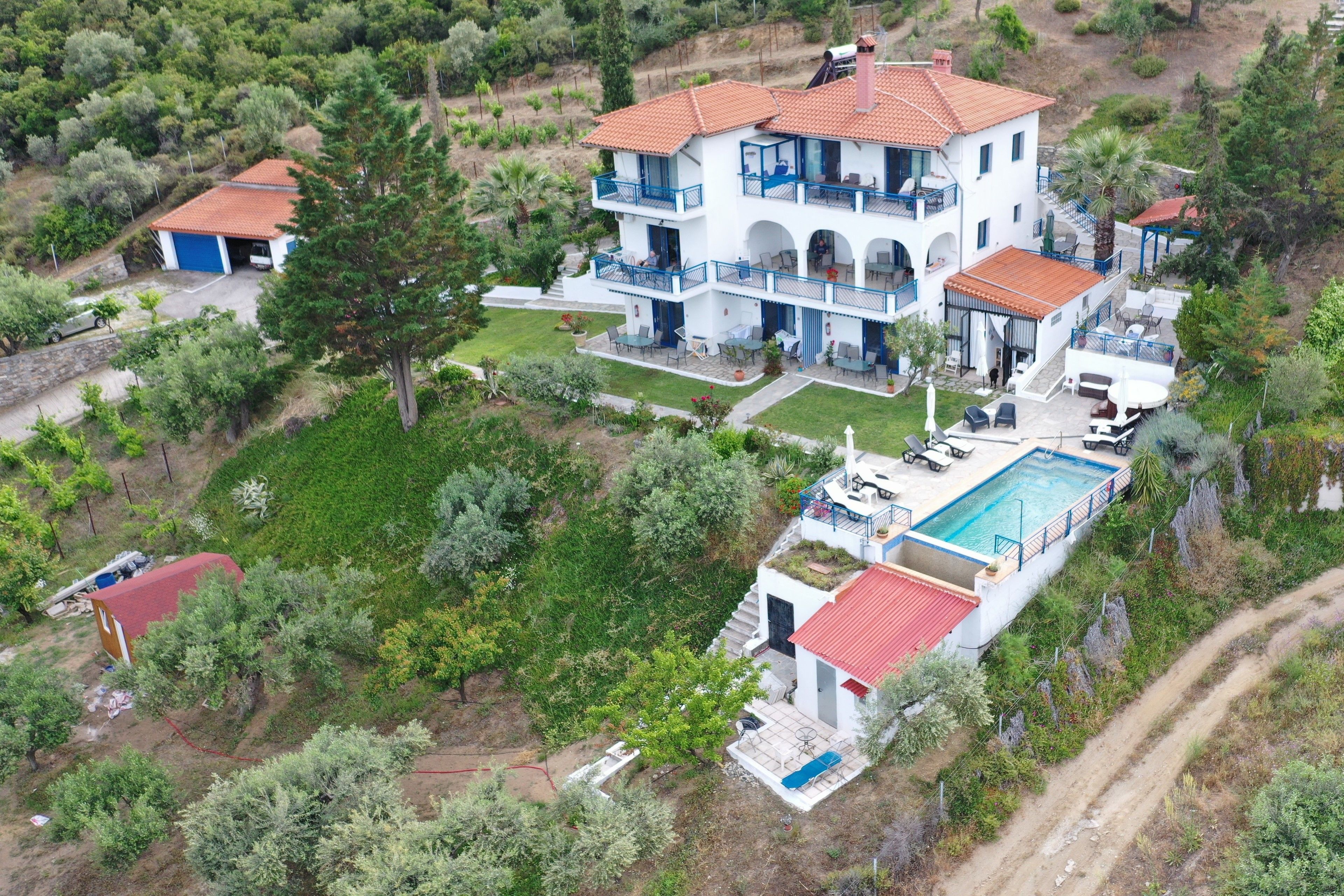 Una casa de dos pisos con piscina, rodeada de follaje y árboles.