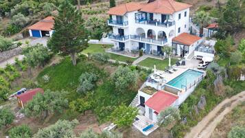 Una casa de dos pisos con piscina, rodeada de follaje y árboles.