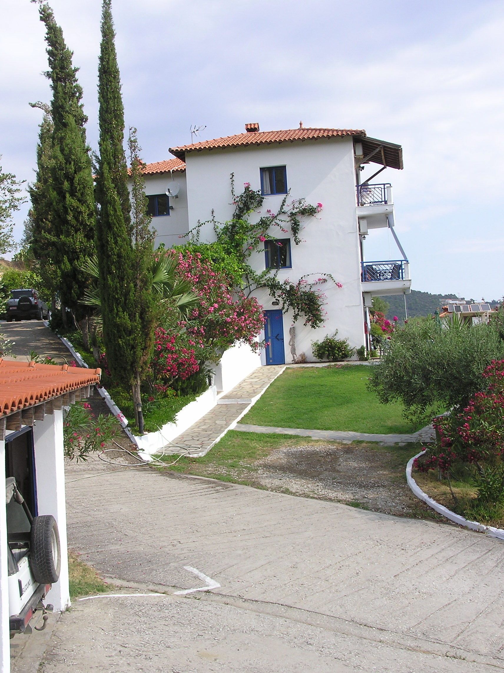 A two-story building with a white facade and a red-tiled roof, a blue door, and a small balcony on the upper floor.