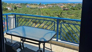 A balcony with a table and chairs, a blue railing, and a view of a green landscape with houses and mountains in the distance. - SartiVista (Sithonia)