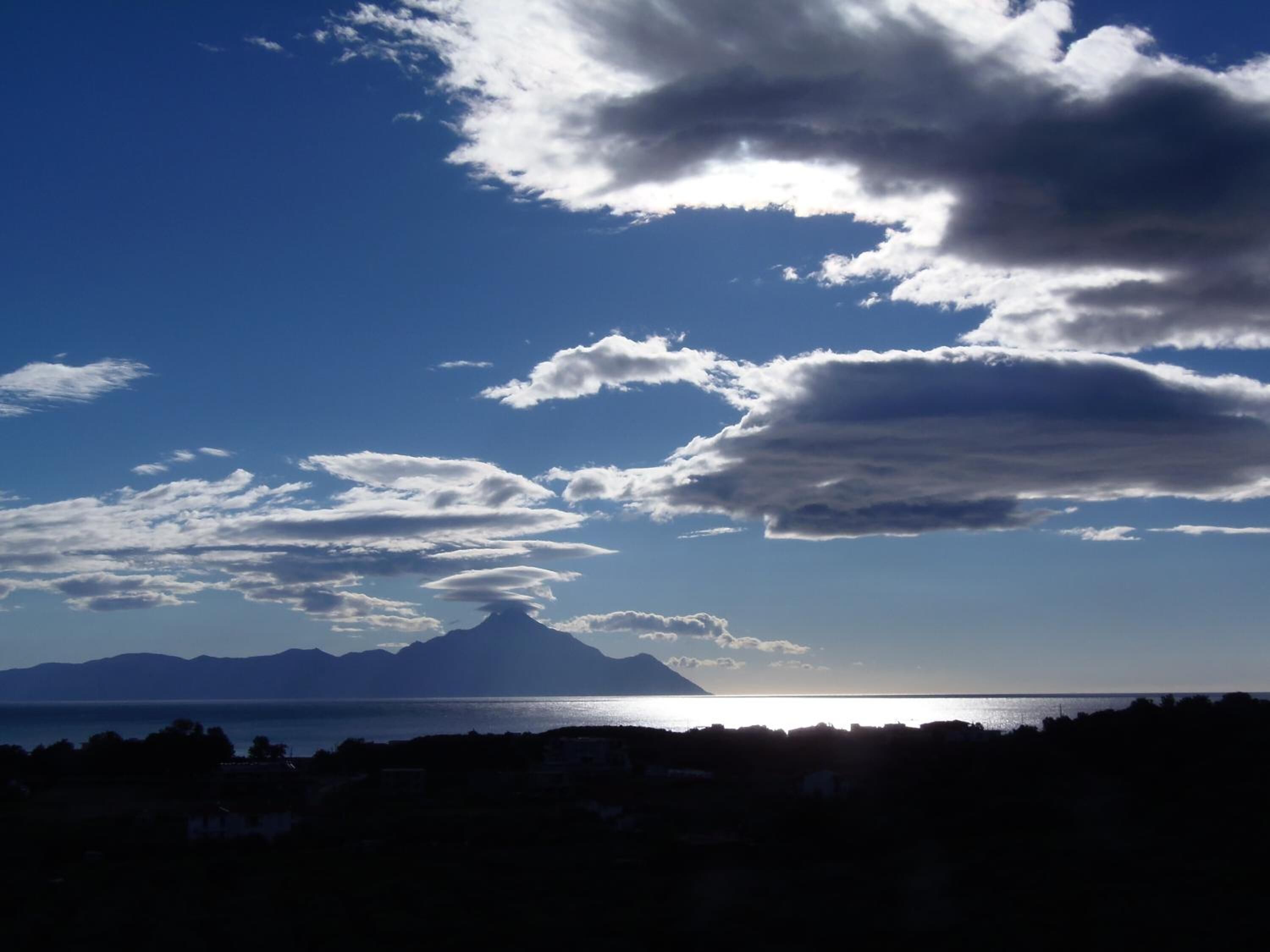 A coastal landscape with a mountain in the distance, a clear sky, and a body of water.