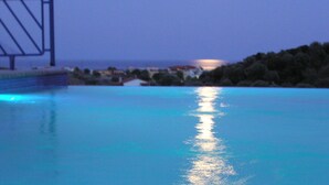 A pool with clear blue water reflecting the moon and distant buildings. - SartiVista (Sithonia)