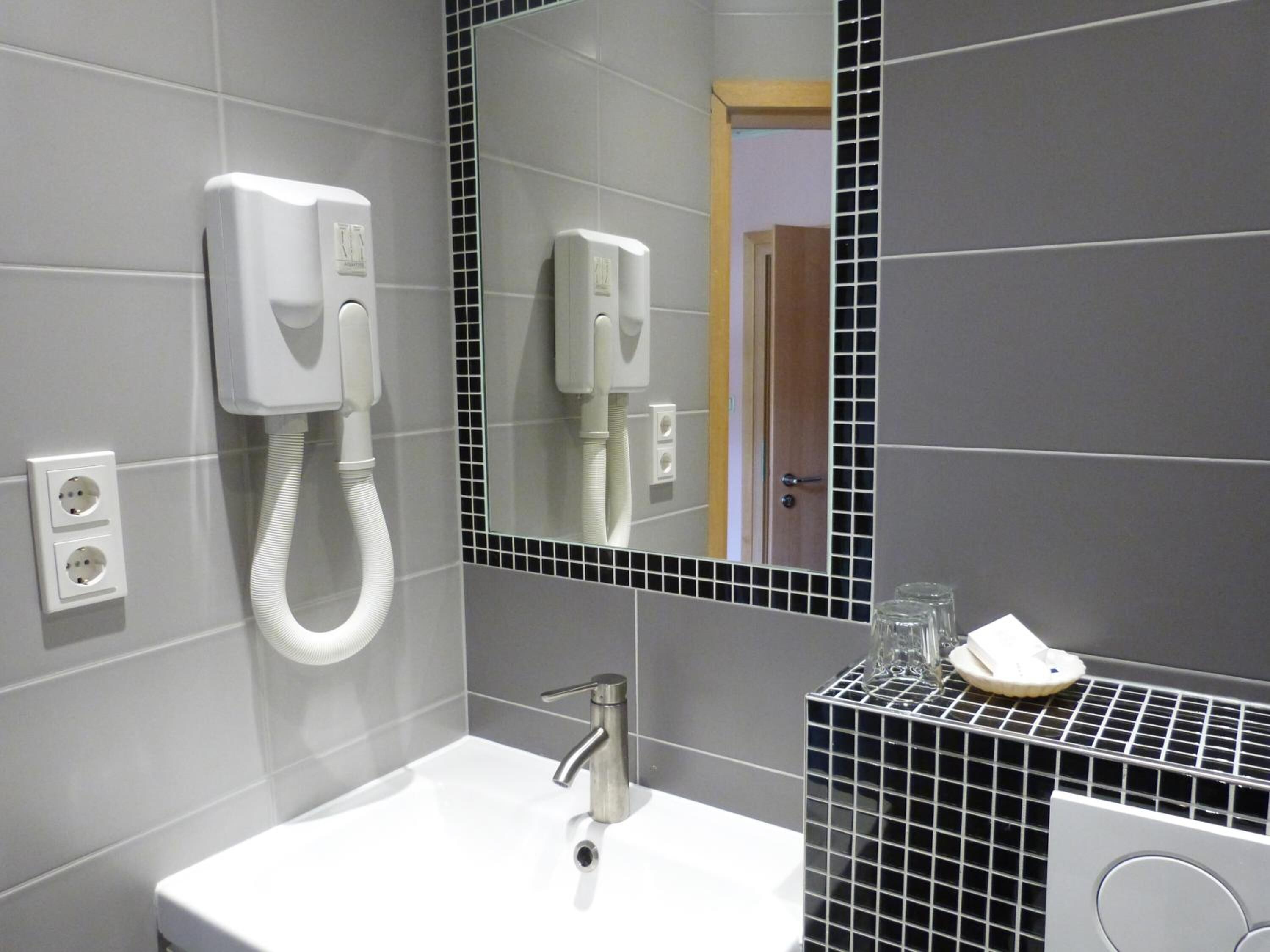 Un baño moderno con un lavamanos blanco, un secador de pelo de mano y un espejo con marco negro.