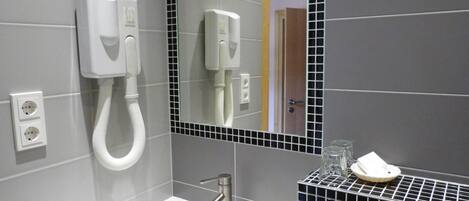 Un baño moderno con un lavamanos blanco, un secador de pelo de mano y un espejo con marco negro.