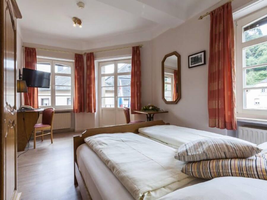 A hotel room with two beds, a desk, a chair, a television, and large windows with curtains.