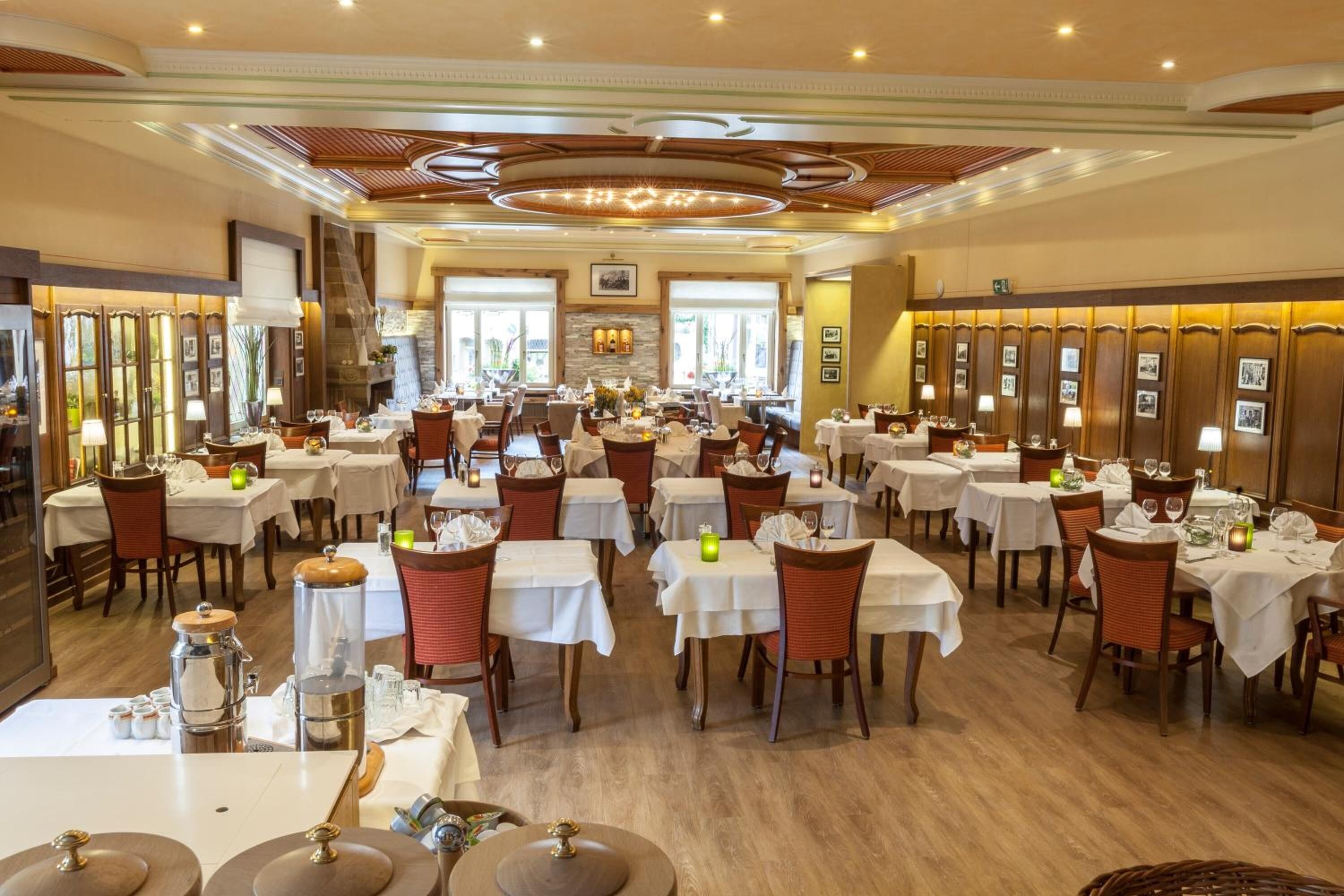 A spacious dining area with multiple tables and chairs, a central fireplace, and framed pictures on the walls.