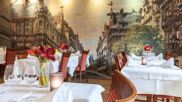 A dining area with tables set for a meal, featuring a view of a street with buildings and a mural on the ceiling. - Hôtel - Restaurant Victor Hugo (Vianden)