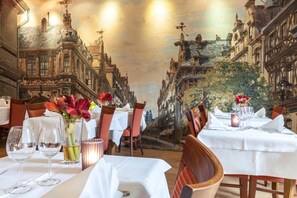 A dining area with tables set for a meal, featuring a view of a street with buildings and a mural on the ceiling. - Hôtel - Restaurant Victor Hugo (Vianden)