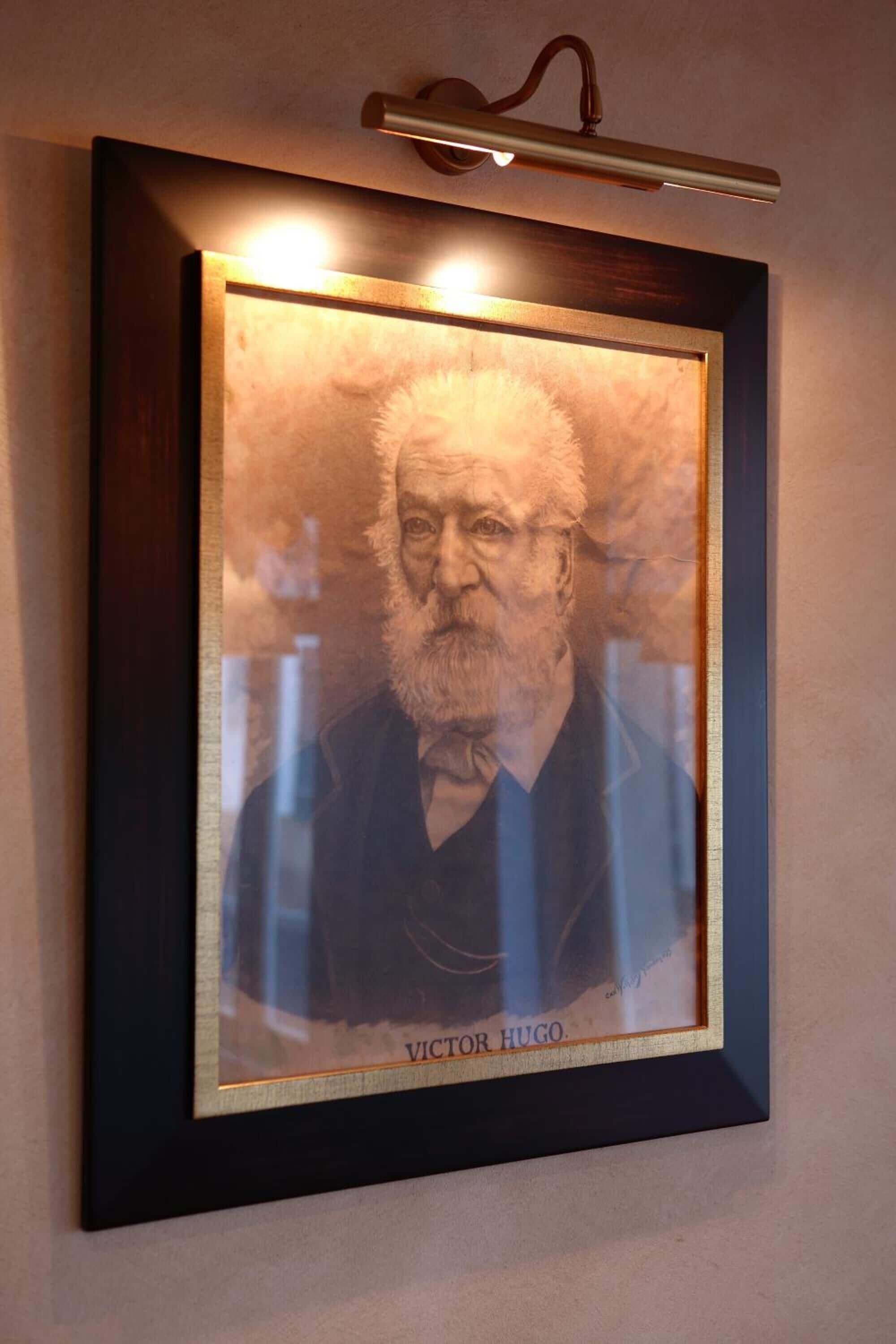 A framed portrait of Victor Hugo with a dark frame and a light fixture above it.