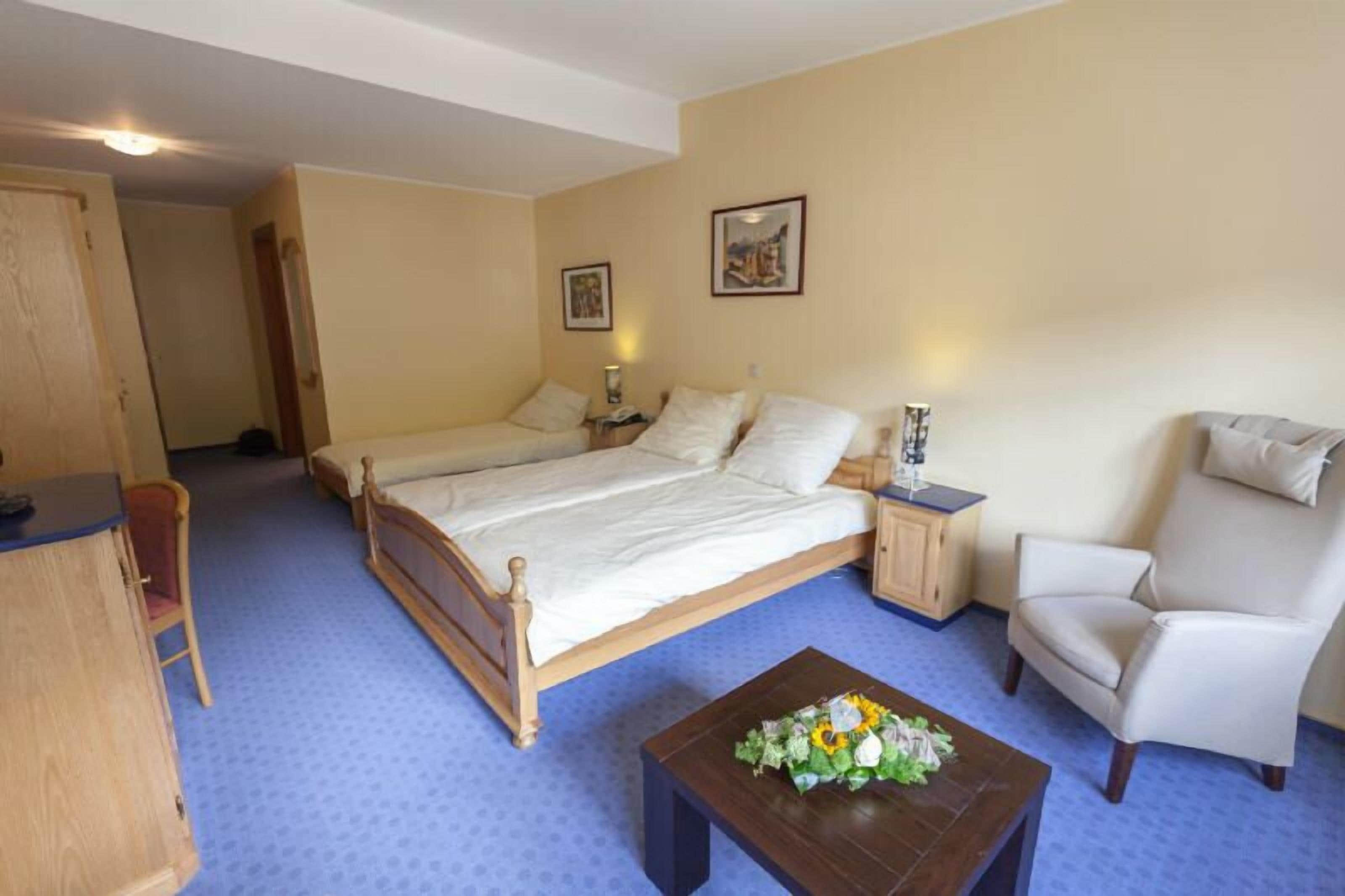 A bedroom with a large bed, a chair, a small table with flowers, and a cabinet.