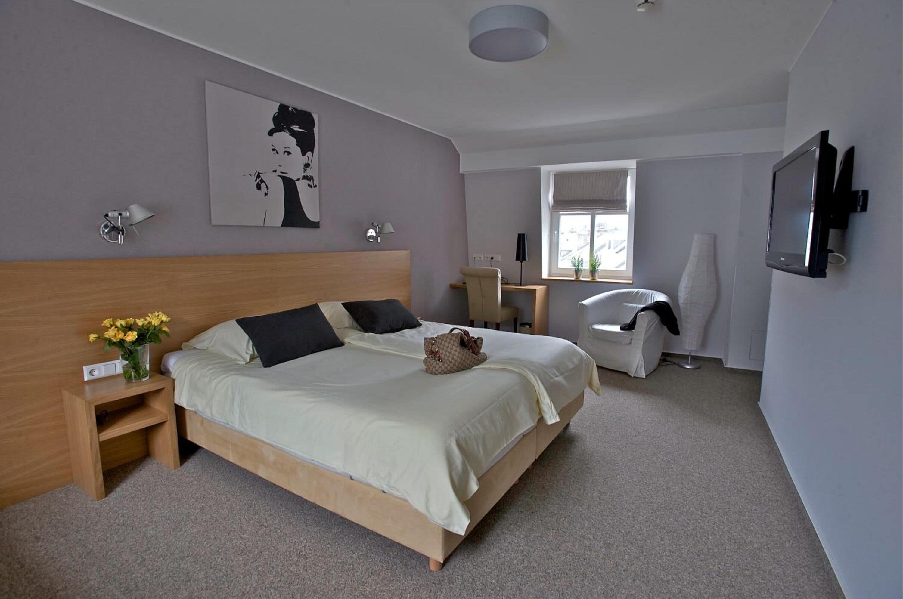 Ein Schlafzimmer mit Bett, Nachttisch, Lampe, Kunstwerk, Fernseher und einem Fenster.