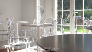 A dining area with clear glass chairs and tables, large windows with a view of greenery, and a door with a handle. - Villa Horti della Fasanara (Ferrara)