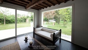 A room with a wooden ceiling, a sofa, and large windows overlooking a garden. - Villa Horti della Fasanara (Ferrara)