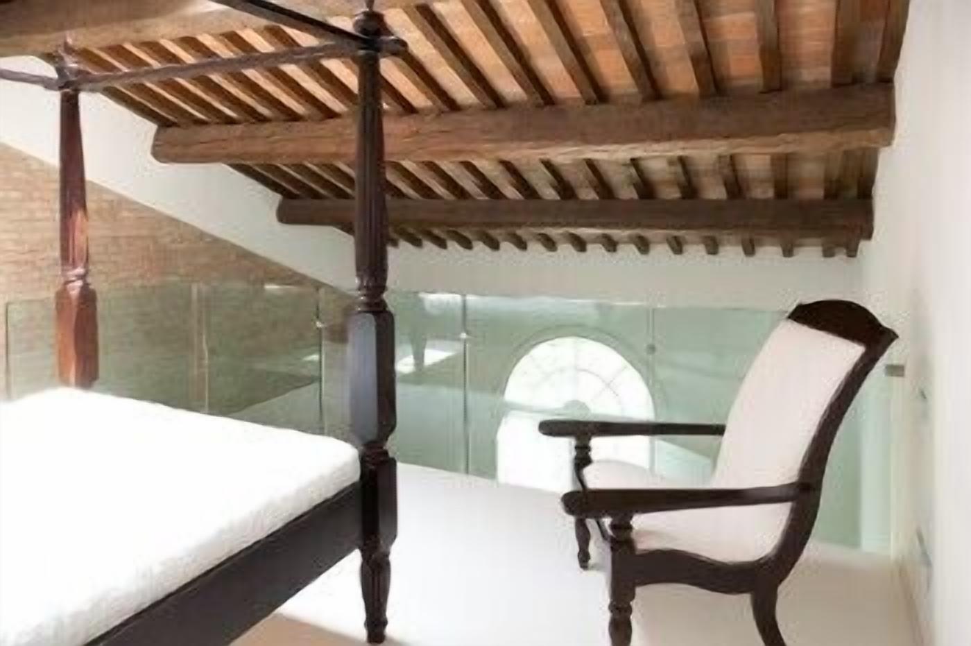 A bedroom with a four-poster bed, a wooden ceiling, and a glass balustrade.