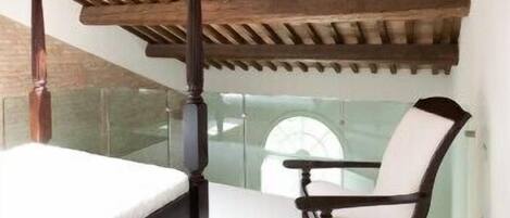A bedroom with a four-poster bed, a wooden ceiling, and a glass balustrade.