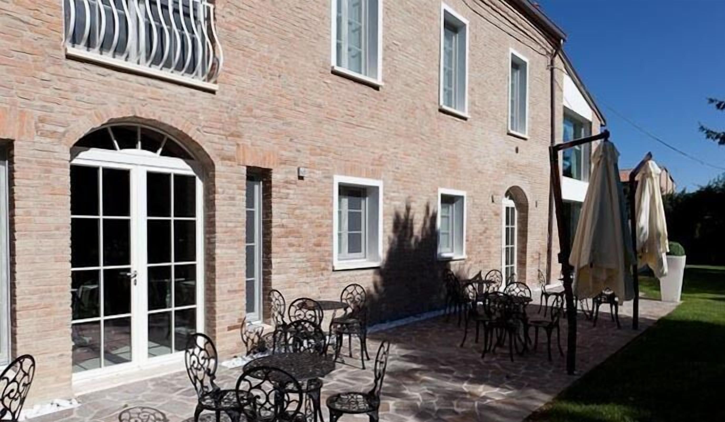 A brick building with a patio area featuring outdoor seating and a large window.